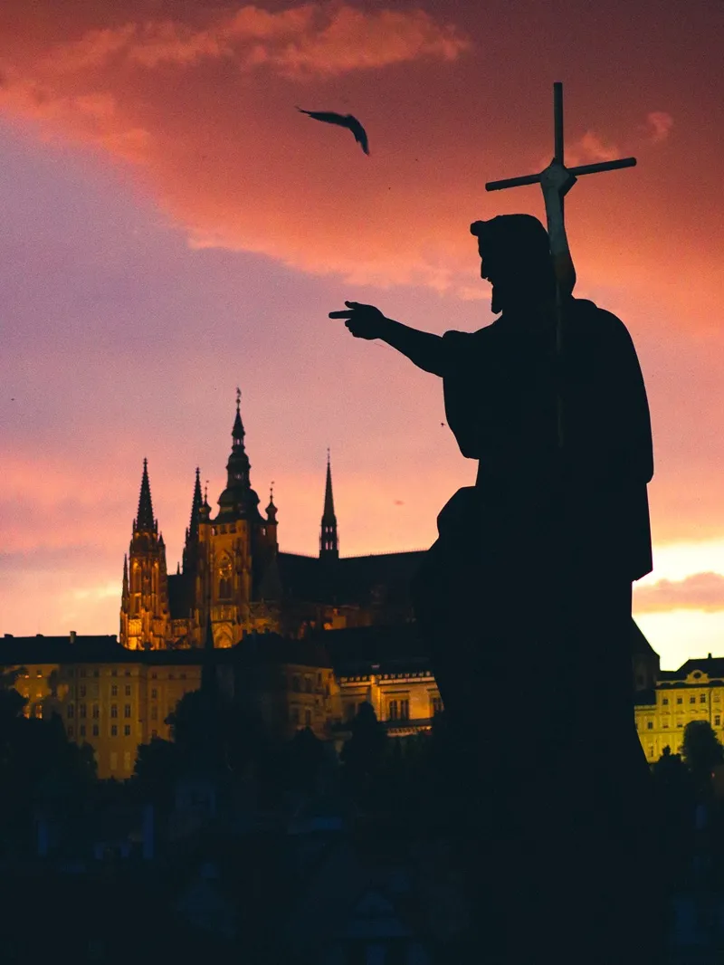 Sylwetka pomnika na tle zachodu słońca i Zamku Praskiego